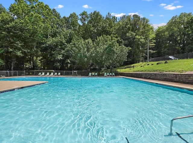 community pool with fence and view of wooded area
