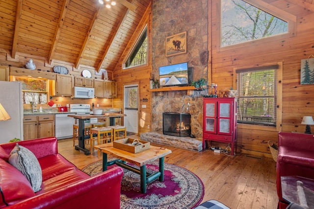 living area with high vaulted ceiling, wooden ceiling, wooden walls, light wood-style floors, and a stone fireplace