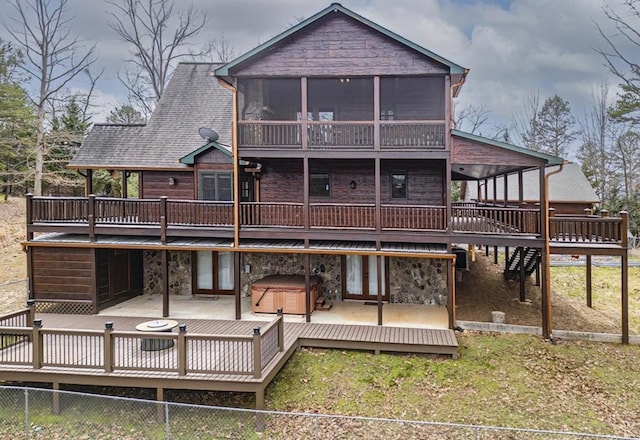 back of property featuring fence, a wooden deck, a sunroom, a hot tub, and stone siding