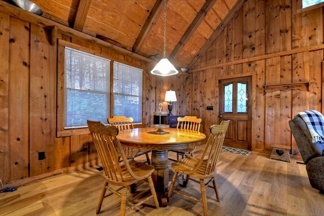 dining room with beamed ceiling, light hardwood / wood-style floors, wooden walls, and a healthy amount of sunlight