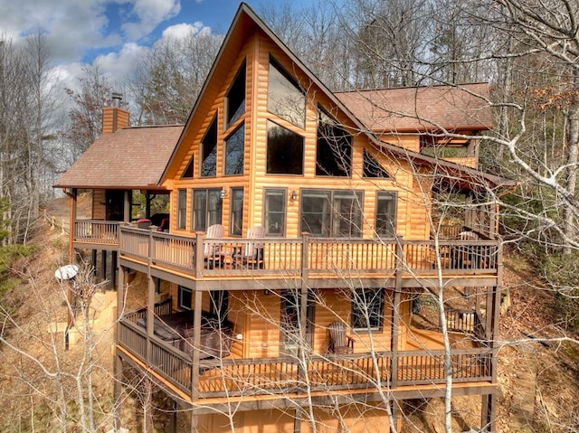 rear view of property featuring log veneer siding, a chimney, and roof with shingles