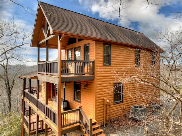 back of house with a shingled roof, central AC unit, a balcony, and faux log siding