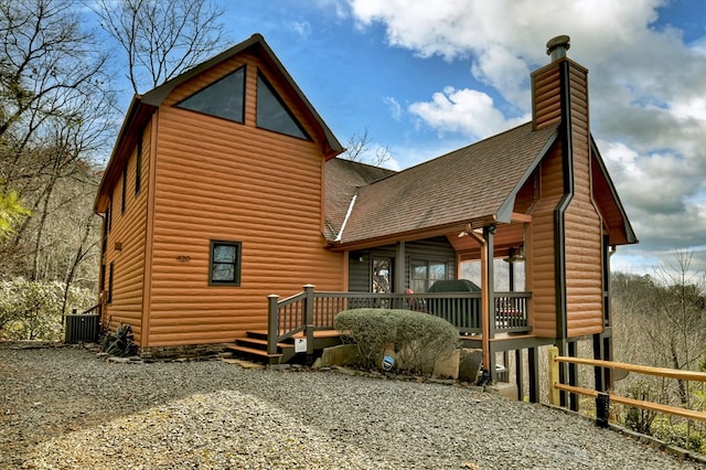 rear view of property featuring cooling unit, faux log siding, roof with shingles, and a chimney