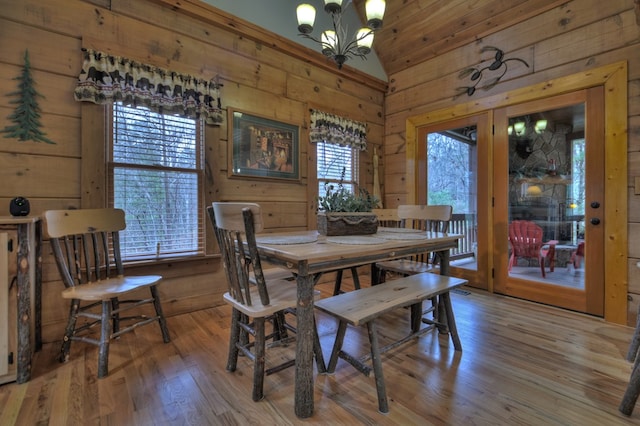 dining space featuring lofted ceiling, wood-type flooring, wooden walls, and a chandelier