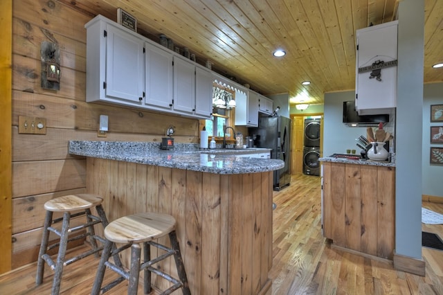 kitchen with kitchen peninsula, light stone countertops, a breakfast bar, and stacked washer / dryer