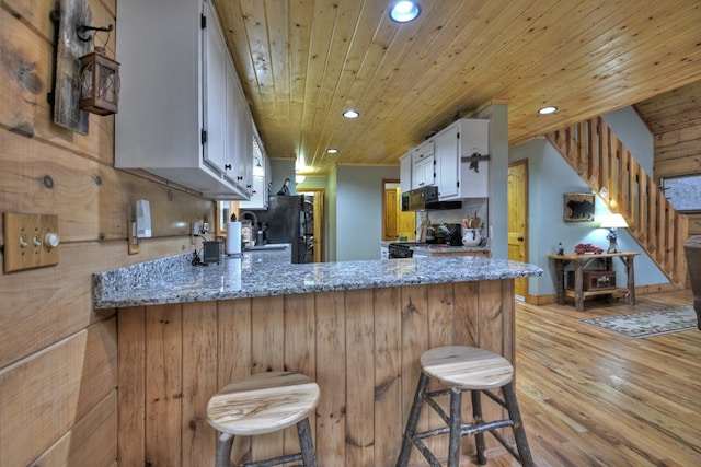 kitchen featuring light stone countertops, white cabinetry, wooden ceiling, and a breakfast bar area