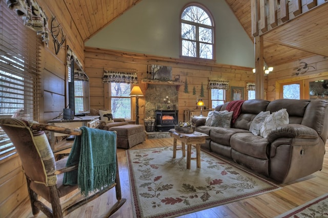 living room featuring hardwood / wood-style floors, wooden walls, a wood stove, and high vaulted ceiling