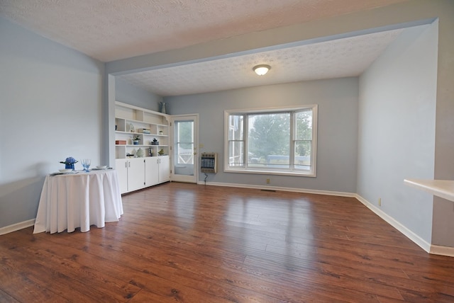 unfurnished living room with dark wood-type flooring, heating unit, and a textured ceiling