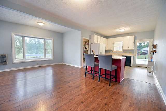 kitchen featuring a breakfast bar area, a center island, dishwasher, white refrigerator with ice dispenser, and white cabinets