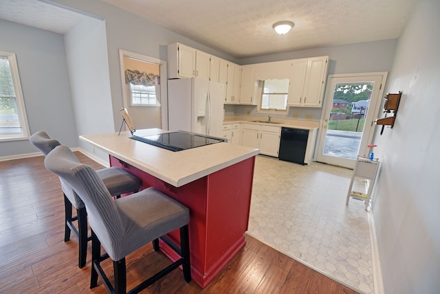 kitchen featuring a breakfast bar, wood-type flooring, black appliances, a textured ceiling, and white cabinets