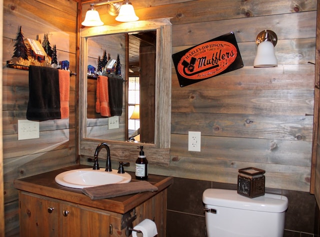 bathroom with vanity, toilet, and wood walls