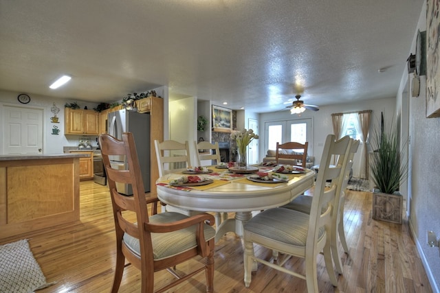 dining space featuring ceiling fan, a textured ceiling, a fireplace, and light hardwood / wood-style flooring