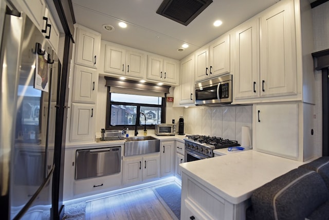 kitchen with white cabinetry, appliances with stainless steel finishes, decorative backsplash, light wood-type flooring, and sink