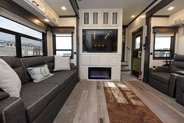 living room with a wealth of natural light, crown molding, and light wood-type flooring