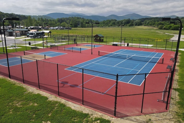 view of tennis court with a mountain view and a lawn