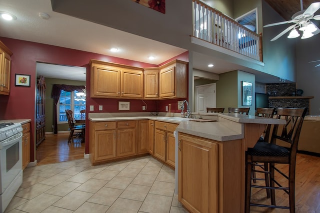 kitchen with a kitchen bar, white range with electric stovetop, sink, kitchen peninsula, and ceiling fan