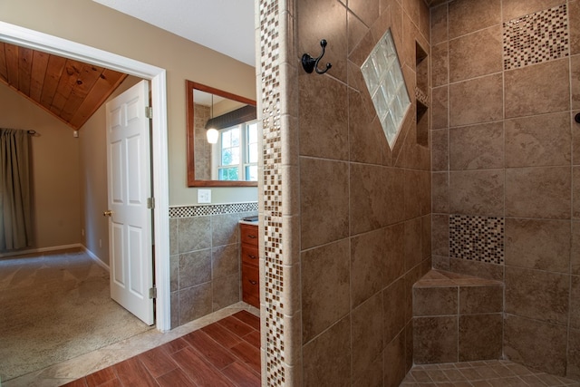 bathroom featuring tile walls, vanity, a tile shower, and vaulted ceiling