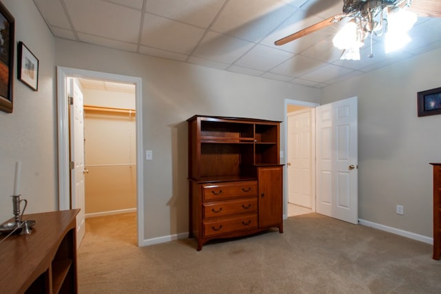 bedroom with ceiling fan, light colored carpet, a paneled ceiling, and a walk in closet