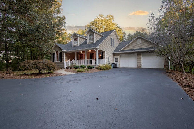 cape cod-style house featuring covered porch and a garage