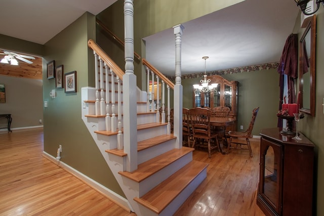 stairway featuring wood-type flooring and ceiling fan with notable chandelier