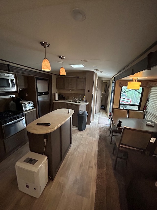 kitchen featuring stainless steel appliances, light hardwood / wood-style floors, dark brown cabinetry, a kitchen island, and decorative light fixtures