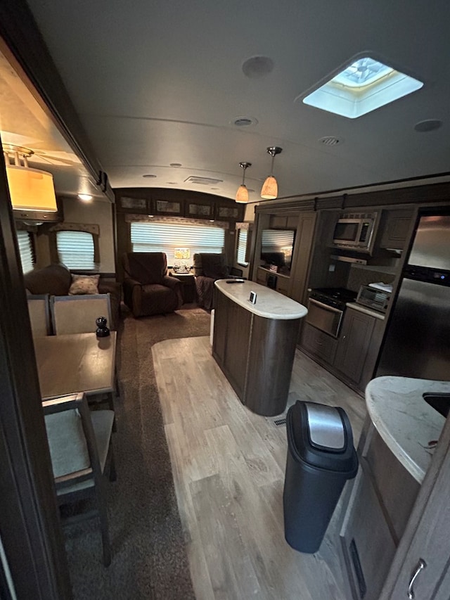 interior space featuring stainless steel appliances, a center island, a skylight, pendant lighting, and light wood-type flooring