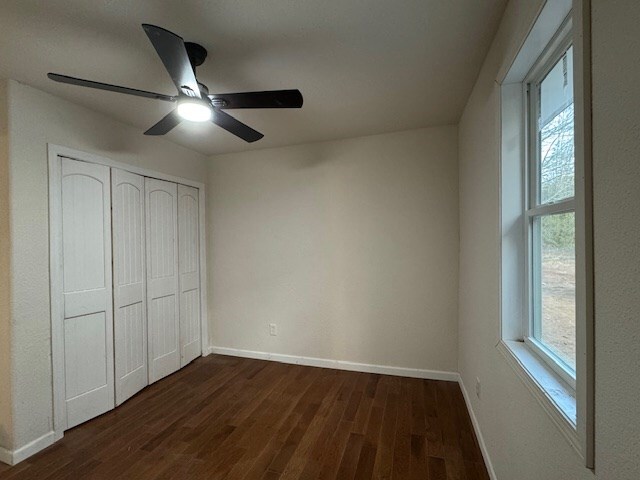 unfurnished bedroom featuring ceiling fan, a closet, dark wood-type flooring, and multiple windows