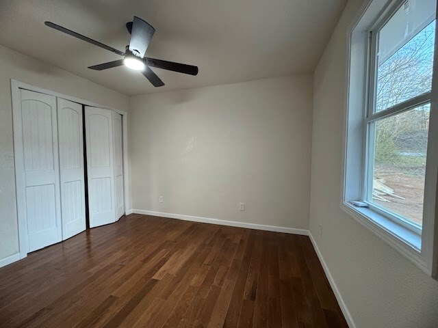 unfurnished bedroom with ceiling fan, a closet, and dark wood-type flooring