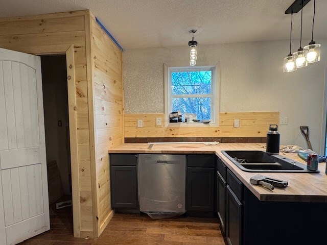 kitchen with dishwasher, sink, dark hardwood / wood-style flooring, decorative light fixtures, and wooden walls