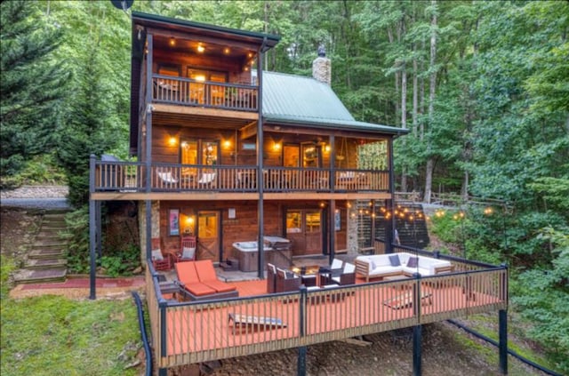 back of house featuring an outdoor living space, a balcony, a hot tub, and a deck