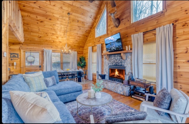 living room with wood walls, high vaulted ceiling, a stone fireplace, hardwood / wood-style flooring, and a notable chandelier