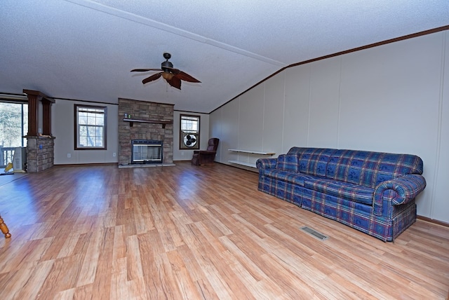 unfurnished living room with a textured ceiling, ceiling fan, light hardwood / wood-style floors, a stone fireplace, and lofted ceiling