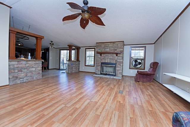 unfurnished living room featuring ceiling fan, a stone fireplace, a textured ceiling, and light hardwood / wood-style flooring