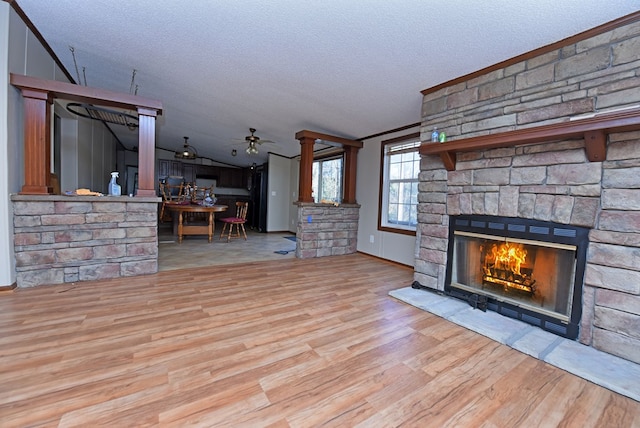 unfurnished living room featuring a stone fireplace, ceiling fan, light hardwood / wood-style flooring, and a textured ceiling