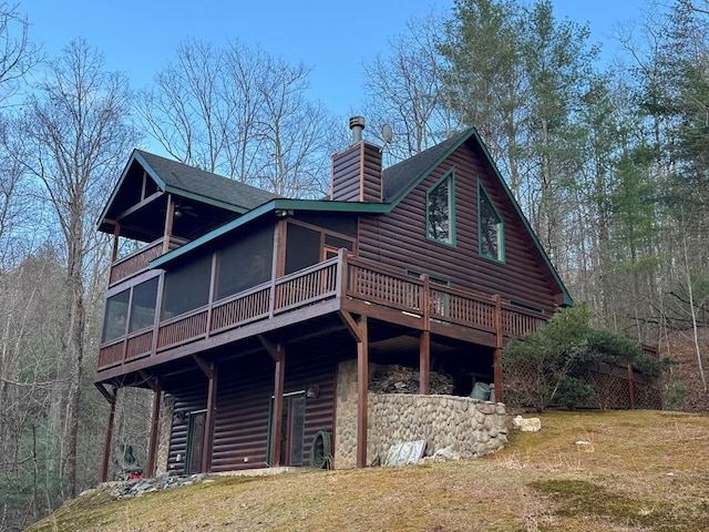 rear view of house with faux log siding, a shingled roof, a sunroom, and a chimney