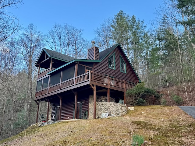 exterior space featuring faux log siding, a chimney, roof with shingles, and a sunroom