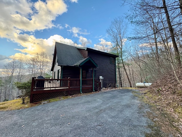 view of side of property featuring a wooden deck, faux log siding, and a shingled roof