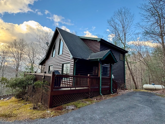 view of front of house featuring a wooden deck, faux log siding, and a shingled roof