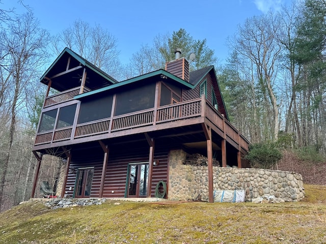 back of house featuring a lawn, french doors, a chimney, a sunroom, and log veneer siding