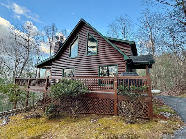 back of house with log veneer siding, a chimney, a deck, and roof with shingles