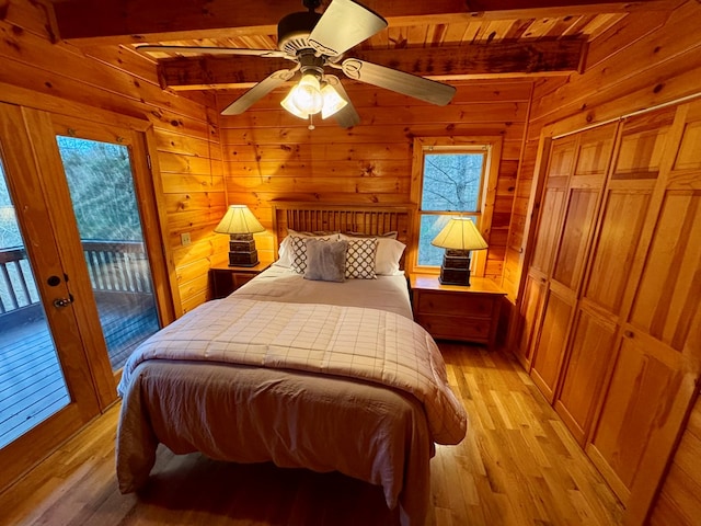 bedroom featuring beam ceiling, wooden walls, light wood-style flooring, and access to outside