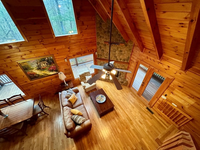 living area with visible vents, beam ceiling, high vaulted ceiling, hardwood / wood-style floors, and wooden walls