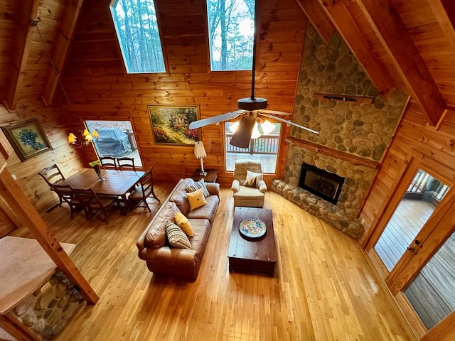 living area featuring a ceiling fan, a healthy amount of sunlight, beam ceiling, a fireplace, and wood-type flooring