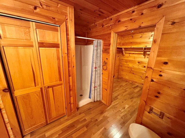 bathroom featuring a shower with shower curtain, wooden walls, wood finished floors, wood ceiling, and toilet