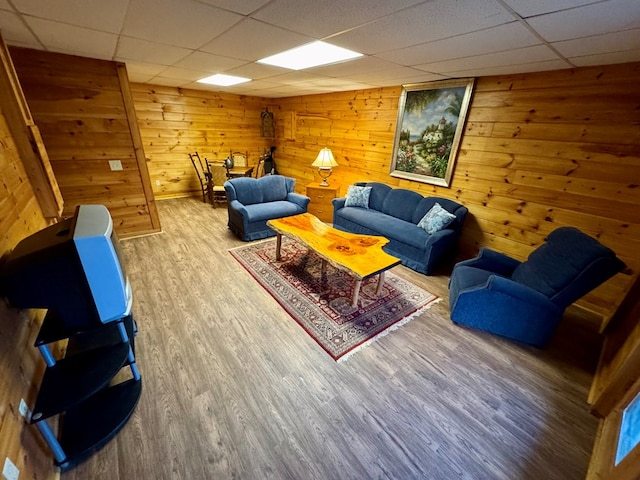 living room with a drop ceiling, wooden walls, and wood finished floors