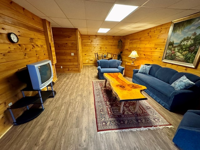 living room with a drop ceiling, wood finished floors, and wood walls