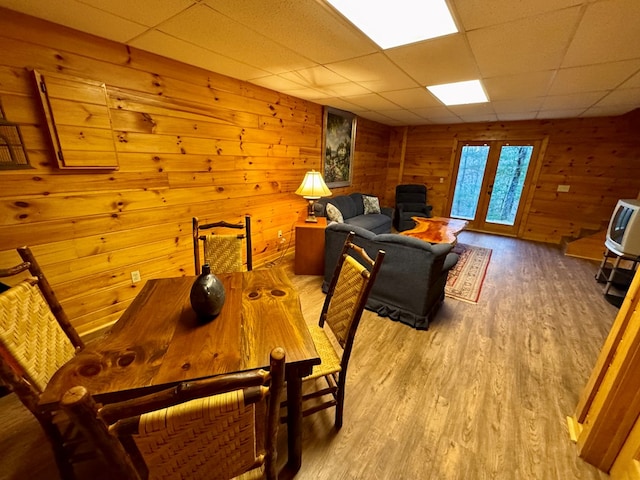 dining space with wooden walls, a drop ceiling, french doors, and wood finished floors