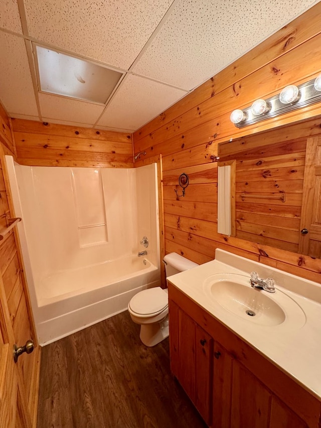 bathroom featuring vanity, wooden walls, wood finished floors, a paneled ceiling, and toilet