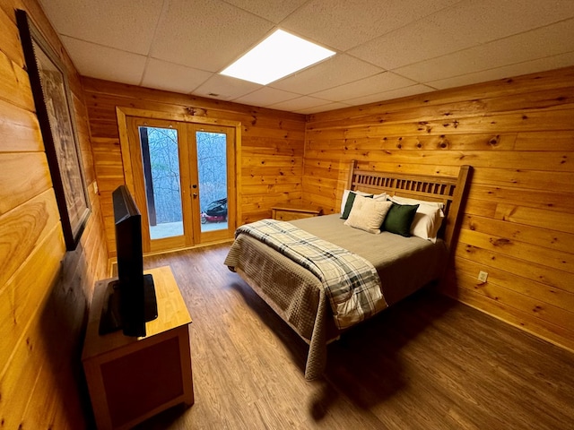 bedroom with french doors, wooden walls, wood finished floors, and access to exterior