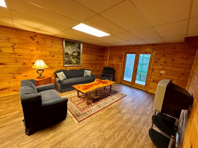 living room with french doors, a paneled ceiling, wooden walls, and wood finished floors